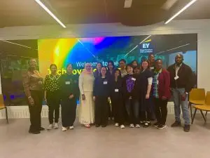 Her Code participants and the AspireHer team gather for a group photo in front of the Technovation welcome screen at EY Wavespace, London.