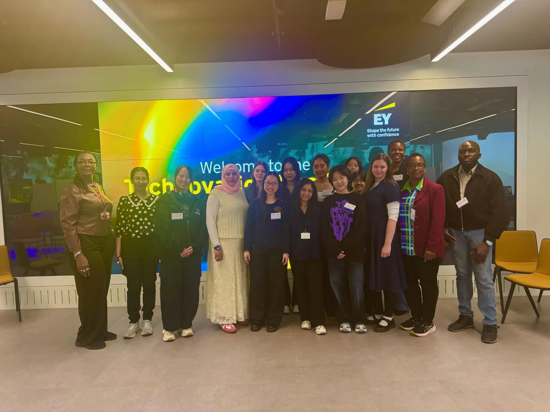 Her Code participants and the AspireHer team gather for a group photo in front of the Technovation welcome screen at EY Wavespace, London.