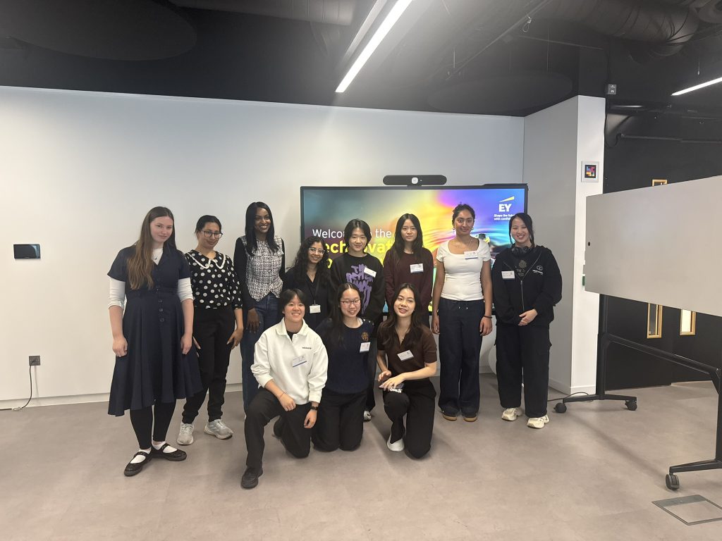 A group of Her Code participants pose together in front of the Technovation screen at EY Wavespace in London.